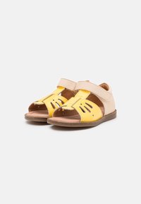 Un paio di sandali aperti per bambini, beige e gialli, con cinturini in velcro, su sfondo bianco.
