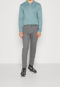 Polo tričko s dlouhými rukávy v světle modré, šedé kalhoty na míru a vícebarevné sportovní boty s tmavými podrážkami a vzorovanými ponožkami.