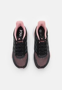 Czarne buty sportowe z siateczkową cholewką i różowymi akcentami, sznurówkami oraz brandingiem. Podeszwa jest biała z teksturowanymi wzorami zapewniającymi przyczepność.