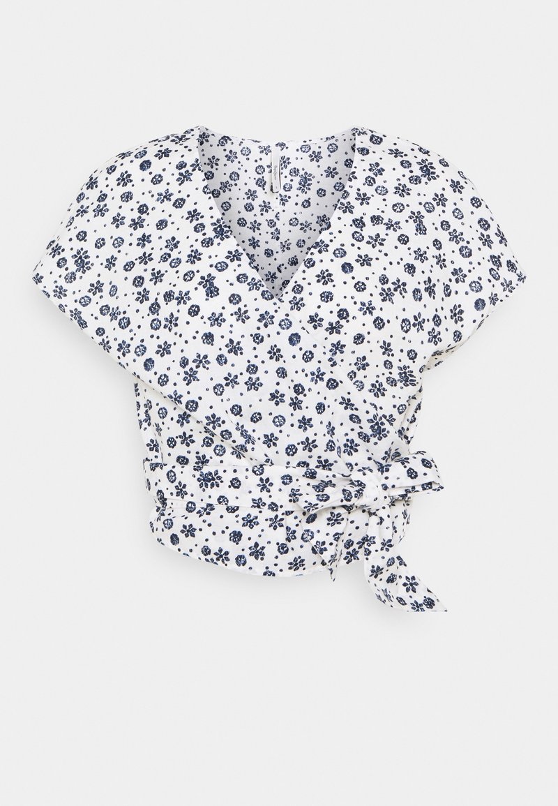 Blouse portefeuille blanche à manches courtes, motif floral et à pois bleu marine, col en V et ceinture nouée sur le côté.