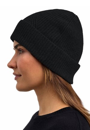 Frau mit schwarzer, gestrickter Mütze mit umgeschlagenem Rand und schwarzem Pullover, im linken Profil vor weißem Hintergrund gezeigt.