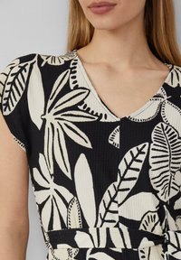 Schwarz-weißes Kleid mit großen Blattmustern, strukturiertem Stoff und V-Ausschnitt. Inklusive eines Gürtels in der Taille für zusätzliche Definition.