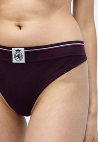 Boxeri din bumbac burgundy, cu un elastic lat la talie, având o dunga albastră și roșie, și un material cu o textură netedă. Plăcuță cu logo în centru.