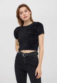 Top corto nero in tessuto peloso con maniche corte, scollo rotondo, indossato con jeans neri a vita alta caratterizzati da dettagli con borchie.