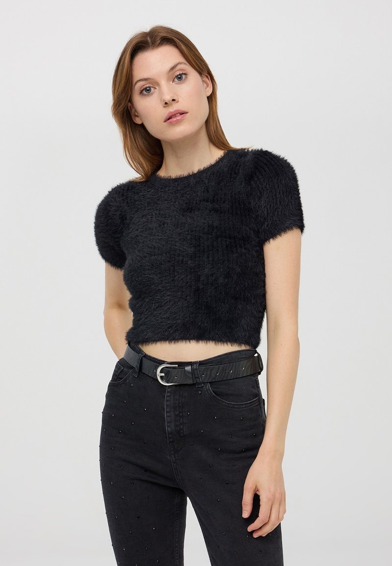 Top corto nero in tessuto peloso con maniche corte, scollo rotondo, indossato con jeans neri a vita alta caratterizzati da dettagli con borchie.