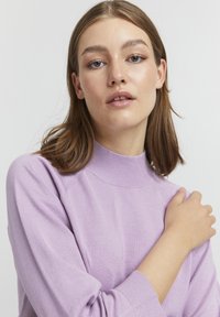 Pull en maille violet clair à manches longues avec un col haut et des poignets côtelés. Texture douce, design ajusté et détails de couture subtils.