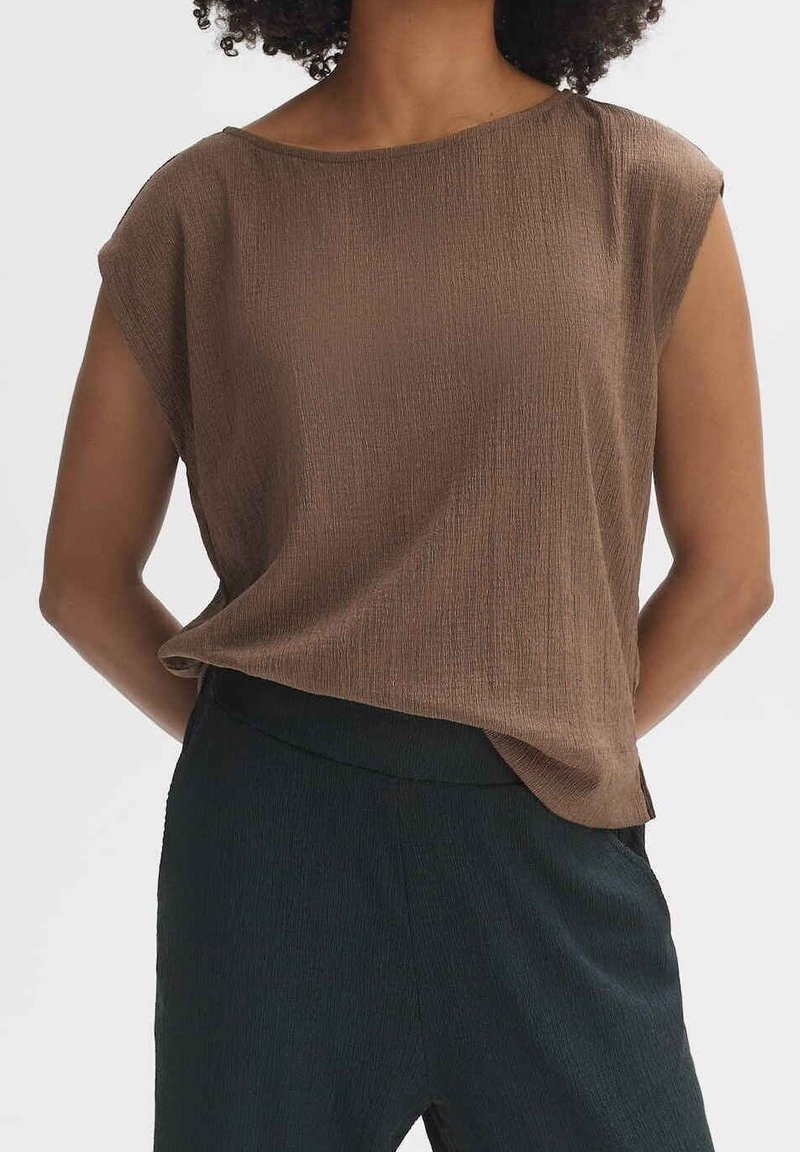 Brun texturerad topp med avslappnad passform, rund halsringning och ärmlöst, kombinerad med mörka, släta byxor.