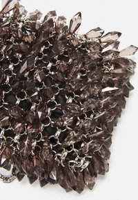 Brązowe koralikowe kryształki ułożone w formie skupiska, przymocowane do srebrnego łańcuszka, z czarnym materiałowym tłem.