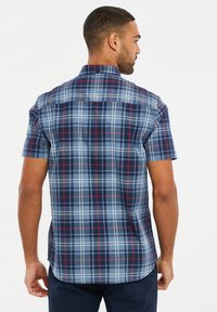 Camisa de cuadros de manga corta en navy, azul claro y blanco con acentos rojos. Presenta un cuello, yugo y dobladillo curvado. Está hecha de una tela ligera.