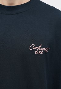 Námořnické bavlněné tričko s kulatým výstřihem a růžovou vyšívanou klasikou "Carhartt WIP" na levé hrudi. Hladká textura, standardní střih.