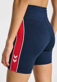 Marinblå sportshorts med hög midja, med röda sidopaneler och vita detaljer, tillverkade av ett mjukt och stretchigt material.