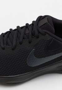 Schwarze Sportschuhe mit einem Obermaterial aus Mesh, runden Schnürsenkeln und einem glatten, schwarzen Nike-Swoosh-Logo an der Seite. Gepolsterte Sohle für Komfort.
