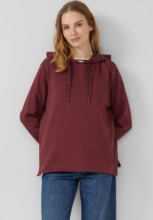 Bordeaux hoodie met een ruim ontwerp, voorzien van een trekkoord capuchon, zijslitsen en zacht textielmateriaal, gecombineerd met blauwe jeans.