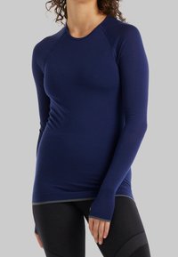 Námořnická modrá dlouhá sportovní tričko s přiléhavým designem, hladkou texturou a otvory na palce na manžetách. Zpevněné švy a kontrastní lem.
