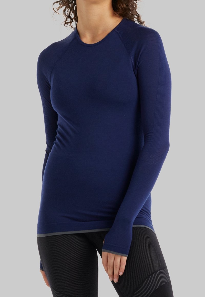 Námořnická modrá dlouhá sportovní tričko s přiléhavým designem, hladkou texturou a otvory na palce na manžetách. Zpevněné švy a kontrastní lem.