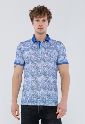 Camisa polo de rayas azules con un diseño texturizado, cuello y puños sólidos de contraste, y una tapeta de tres botones. Se lleva con jeans oscuros.
