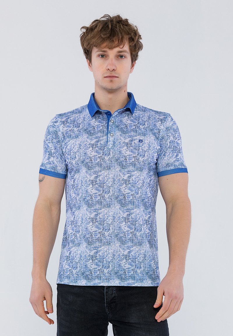 Blå mønstret polo skjorte med en tekstureret design, kontrastfarvet krave og manchetter, samt en tre-knaps lukning. Båret med mørke jeans.