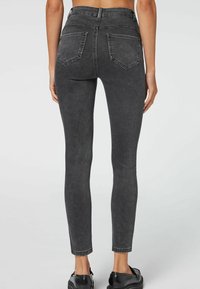 Vaqueros ajustados de mezclilla negra con una cintura alta, diseño de cinco bolsillos y un leve desgaste. Presentan costuras visibles y una textura suave.