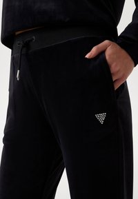 Zwarte velours joggingbroek met elastische tailleband en verstelbaar trekkoord. Voorzien van zijzakken en een driehoekige strassteendecoratie.