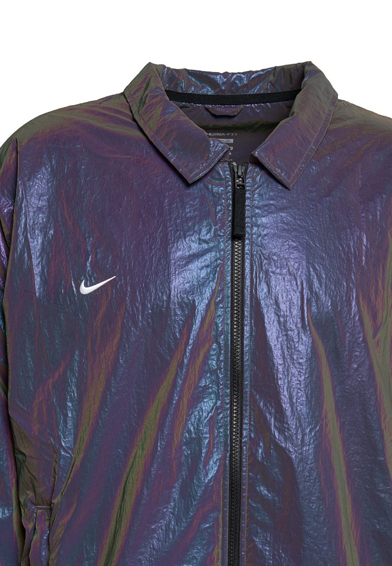 Giacca zip-up viola riflettente con colletto e piccolo logo Nike a forma di swoosh bianco sul lato sinistro del petto.
