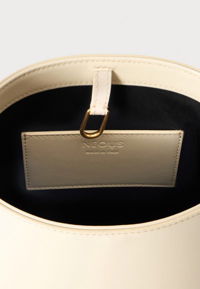 Intérieur de sac à main en cuir beige avec une étiquette cousue indiquant "NEOUS Made in Italy" et une boucle métallique dorée fixée à une lanière en cuir.