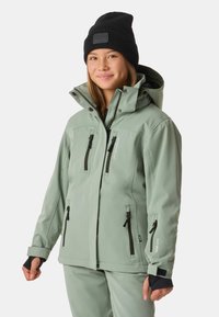 Jasnozielona wodoodporna kurtka z wieloma kieszeniami zapinanymi na zamek i regulowanym kapturem. Czarna czapka dodaje kontrastu do stylizacji. Gładka tekstura.