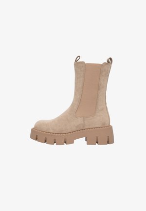 Bottine en suède beige avec des panneaux latéraux élastiques, une semelle épaisse et des languettes au dos. Texture lisse avec des coutures renforcées.
