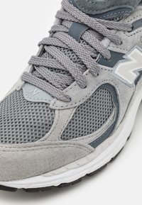 Gray athletic shoe featuring mesh and suede materials, round toe, textured laces, and a patterned rubber sole. Accented with a white logo.