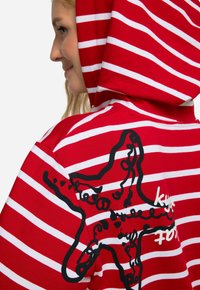 Felpa a righe rosse e bianche con un design astratto nero sul retro. Tessuto morbido con cappuccio regolabile.