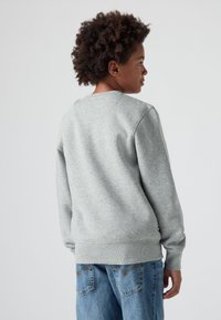 Šedá mikina s kulatým výstřihem a žebrovanými manžetami. Vyrobena z měkké tkaniny, nabízí pohodlný střih. Spárována s modrými džínami.