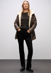Brun, shearling-fodrad jacka över en svart, leopardmönstrad topp; kombineras med svarta raka jeans och svarta ankelboots.