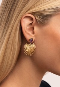 Pendientes de oro con un diseño texturizado de explosión solar y una piedra púrpura central, que exhiben detalles intrincados y una forma audaz.