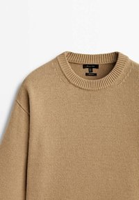 Pull beige en maille avec col rond côtelé et détail de couture d’épaule, posé à plat sur un fond blanc.