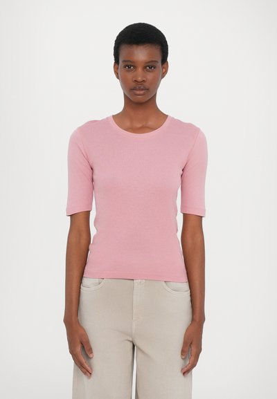 Rosa, kurzärmeliges T-Shirt mit Rundhalsausschnitt, aus weichem Stoff. Kombiniert mit hellbeigen, hochtaillierten Hosen.