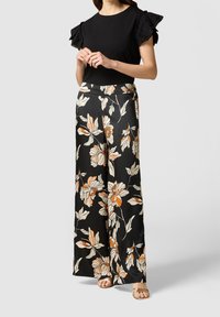 Haut noir avec des manches volantes, associé à un pantalon noir à jambes larges arborant un motif floral en orange et crème. Textures lisses, design élégant.