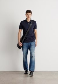 Jūrinės spalvos polo marškiniai, šviesiai mėlyni džinsai, juodi batai ir juoda petinė rankinė. Apranga yra kasdienė ir prigludusi, su lygiu audinio tekstūru.