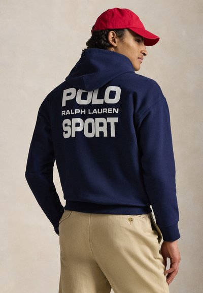 Hanorac bleumarin cu șnur, cu un text mare alb pe spate, care spune „POLO RALPH LAUREN SPORT.” Material neted, manșete ribrate.