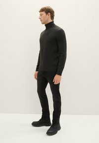 Dunkler Rollkragenpullover kombiniert mit schwarzen Jeans und schwarzen Schuhen. Der Pullover verfügt über einen gerippten Kragen und ein figurbetontes Design.