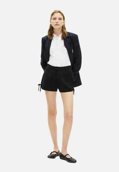 Zwarte shorts met een drawstring, gecombineerd met een witte blouse met kraag. Bovenop een marineblauwe gestreepte blazer met een gouden embleem. Zwarte ballerina's.