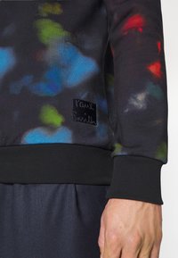 Sudadera negra con patrones abstractos y coloridos. Cuenta con puños y dobladillo acanalados, y una etiqueta negra de felpa con "Paul Smith" en letras en relieve.