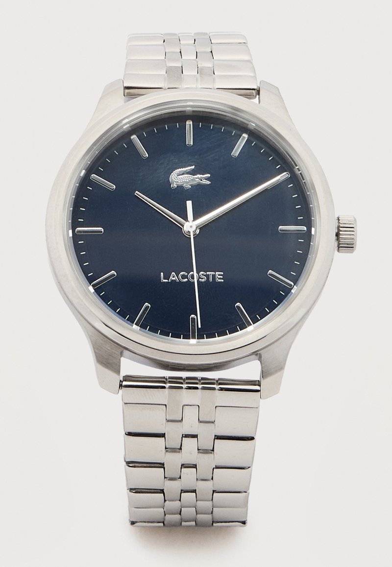 Montre-bracelet en acier inoxydable argenté avec un cadran bleu foncé, des index argentés, trois aiguilles et le logo Lacoste au-dessus du centre.