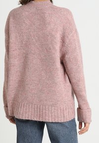 Oversized pinker Pullover aus weichem, strukturiertem Stoff mit hohem Kragen, gerippten Bündchen und Saum für zusätzliche Details.