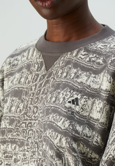 Nærbilde av en person som bruker en teksturert grå og hvit mønstrede hettegenser med et sirkulært Adidas-logo på brystet.