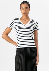 Stripet kortermet V-hals t-skjorte i off-white og marineblå. Mykt stoff, tettsittende design. Lite logo detalj på brystet. Pairt med en svart plissering skjørt.