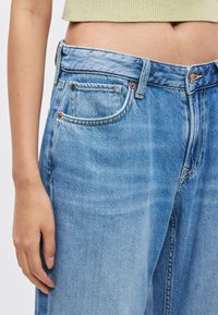 Svijetloplave traperice svijetloplave boje s visokim strukom, pet džepova, detaljima šavova i naglascima od metalnih ukrasa.