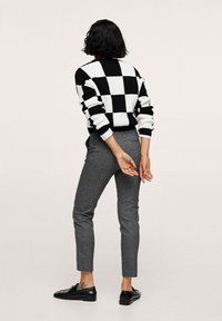 Czarny i biały sweter w kratę z dzianiny o rypsowym wykończeniu, zestawiony z szarymi spodniami slim fit i czarnymi mokasynami. Minimalistyczny design.