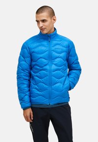 Giacca isolante blu con motivo trapuntato, colletto alto e chiusura con zip. Tessuto liscio con un design leggero e imbottito per mantenere il calore.