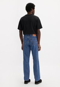 Zwarte t-shirt met korte mouwen, gecombineerd met blauwe straight-leg jeans met achterzakken en een leren label op de tailleband. Zwarte schoenen.
