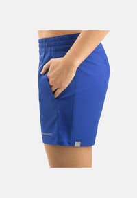 Pantaloni sportivi blu con vita elastica, dettagli con tasche laterali, realizzati in tessuto leggero. Presentano un logo riflettente sull'orlo.