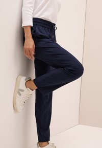 Pantalones de enfoque navy con cintura elástica y cordón ajustable, que cuentan con bolsillos laterales, combinados con zapatillas blancas con detalles grises.